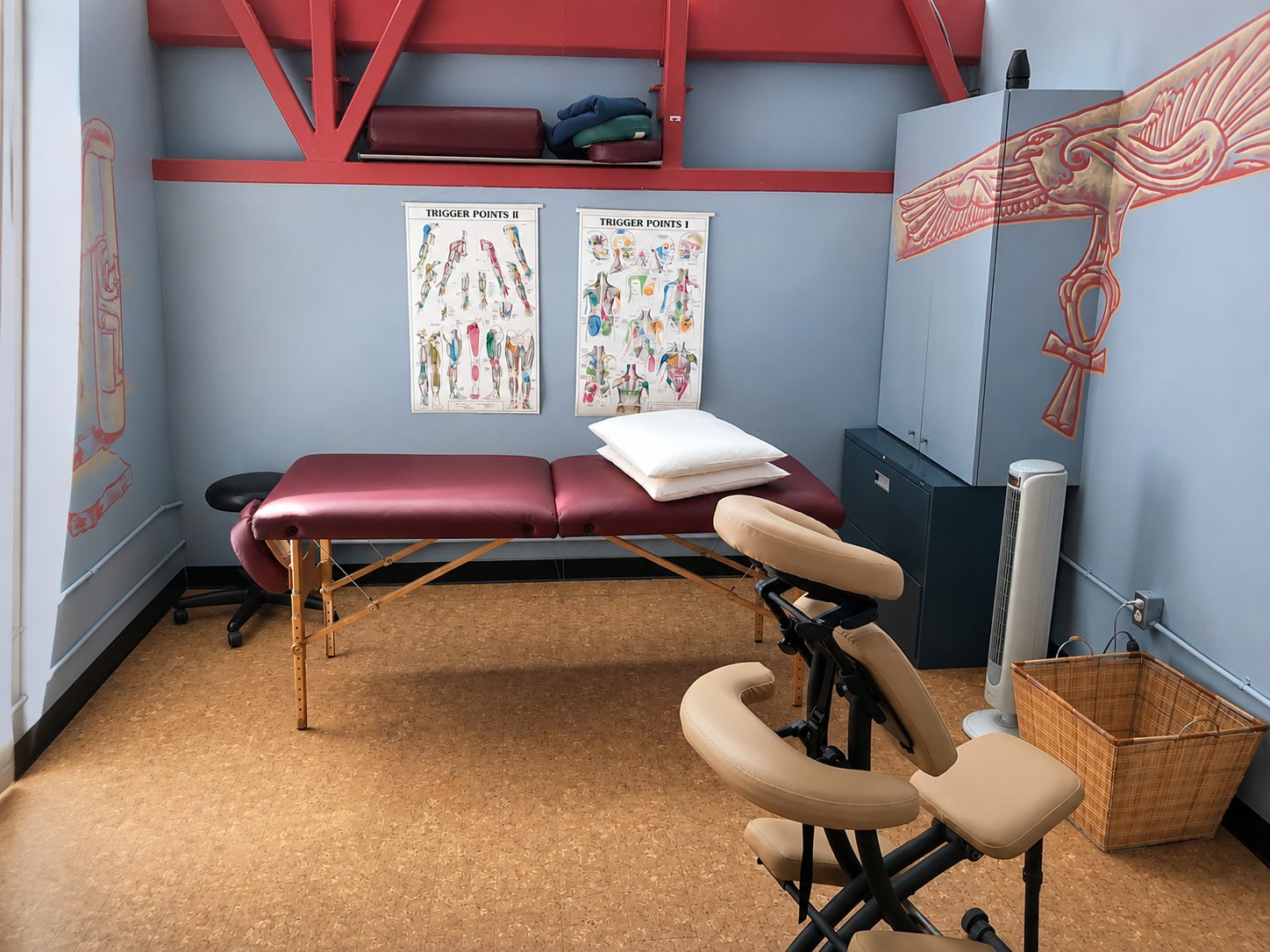 Massage treatment room with a table and chair beneath a hand-painted Horus falcon and ankh mural