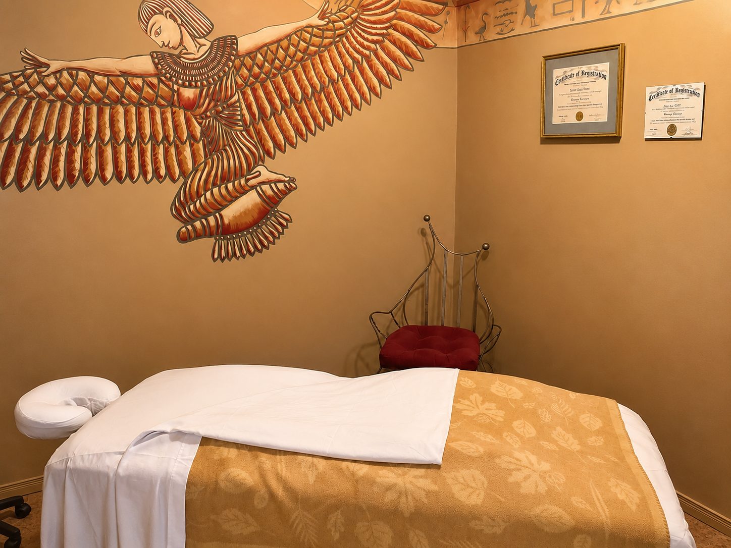 Warm treatment suite with a winged goddess mural above the massage table at Carpe Diem